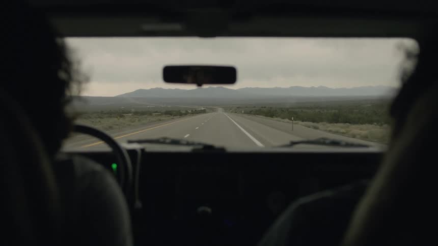 A woman drives a car down a two-lane desert highway