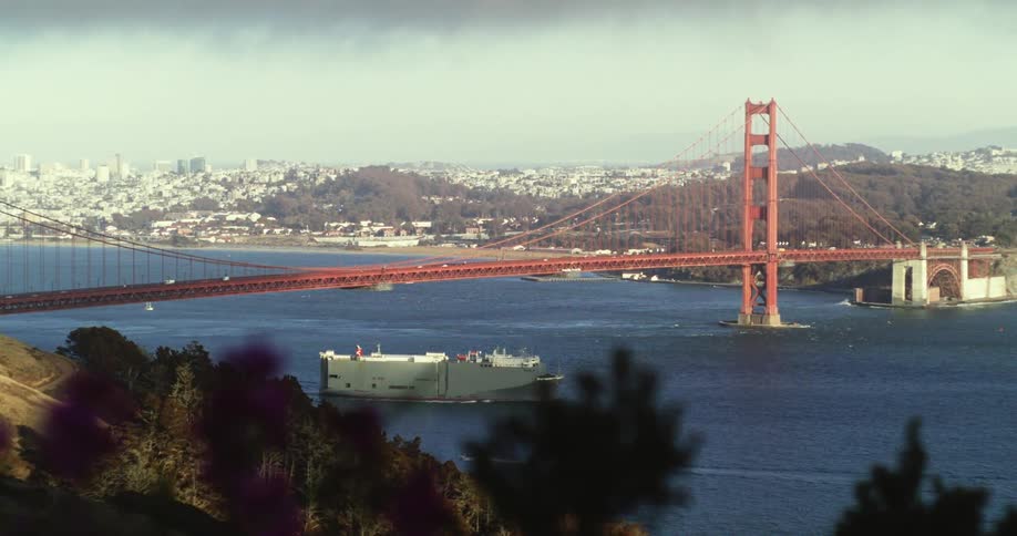 Tracking shot with foreground of the Golden Gate Bridge and San Francisco Panorama of the san francisco bridge with a naval ship passing by and a city in the background