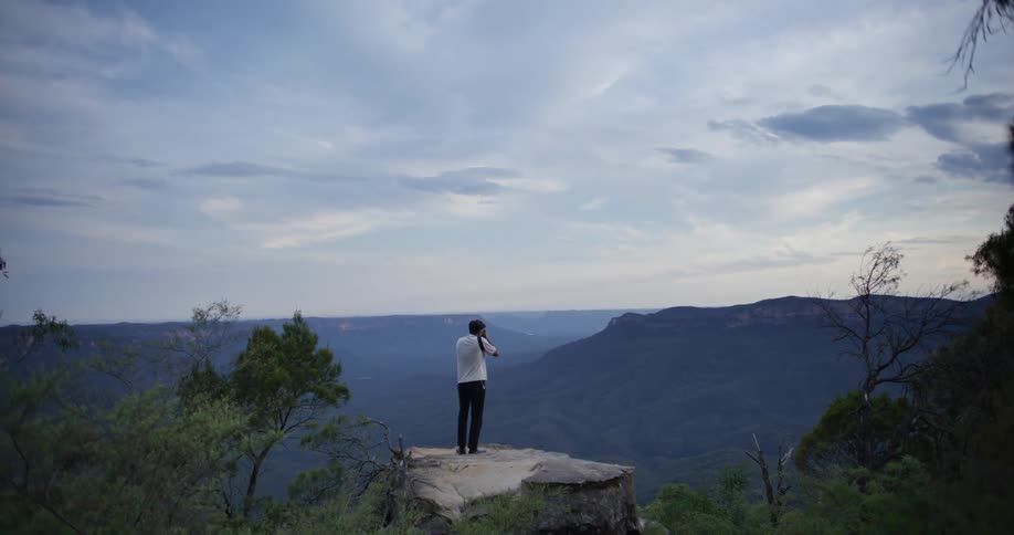 Man on top of a rock photographing a mountain landscape