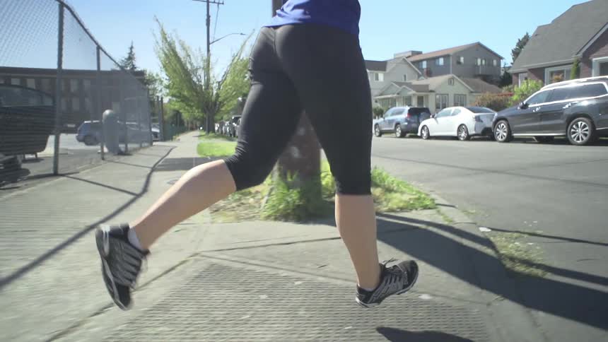 Woman jogging down a sidewalk on a sunny day