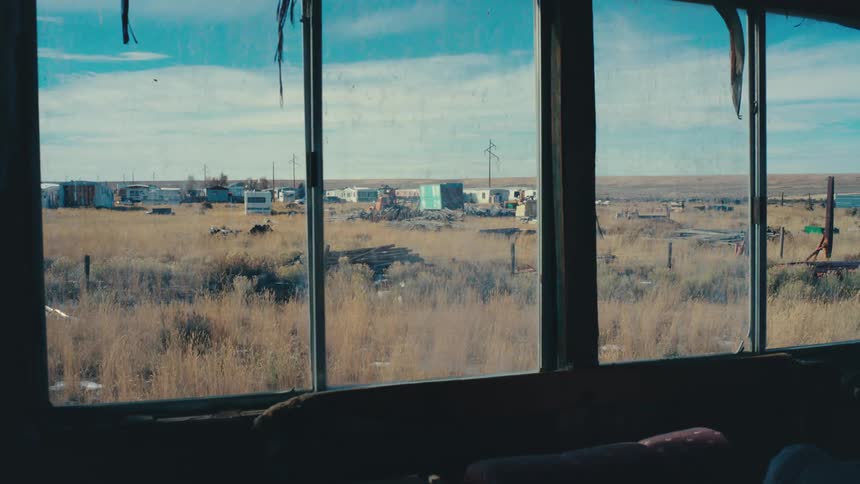 View from the interior window of an abandoned vehicle with cars and houses in the background in sparse vegetation