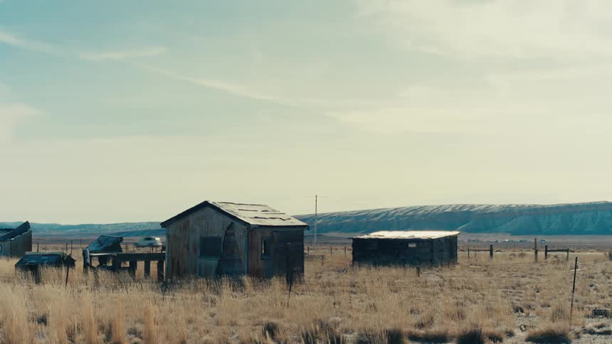 Simple wooden houses in a field with mountains in the background