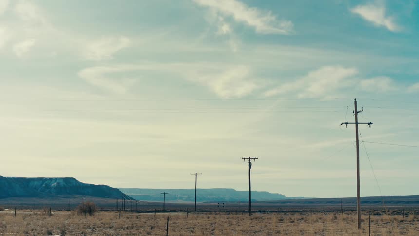 Line of utility poles crosses a highway passing through the rural countryside on a cloudy day