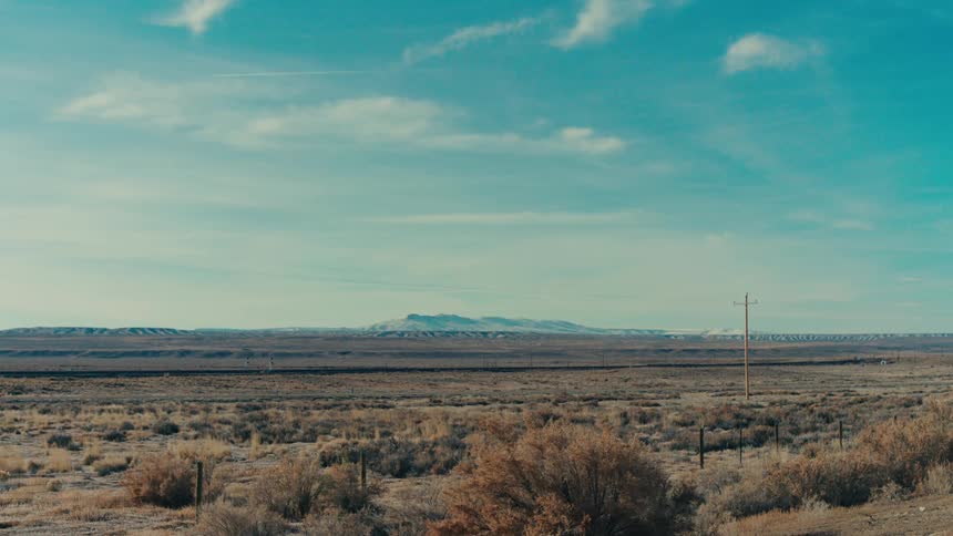 A vast open landscape stretches towards a distant mountain range with a train track cutting through the arid terrain