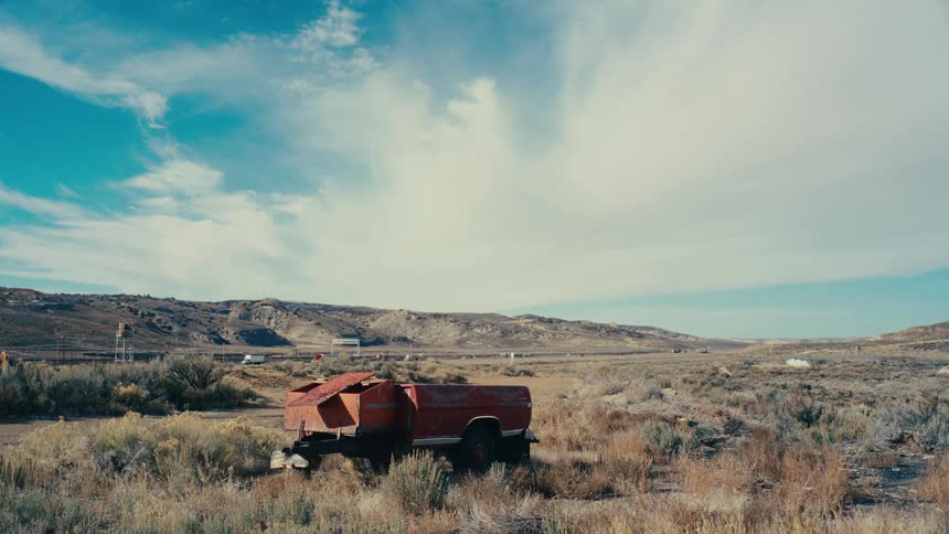Red vehicle in the middle of desert vegetation and in the background a highway with vehicle traffic