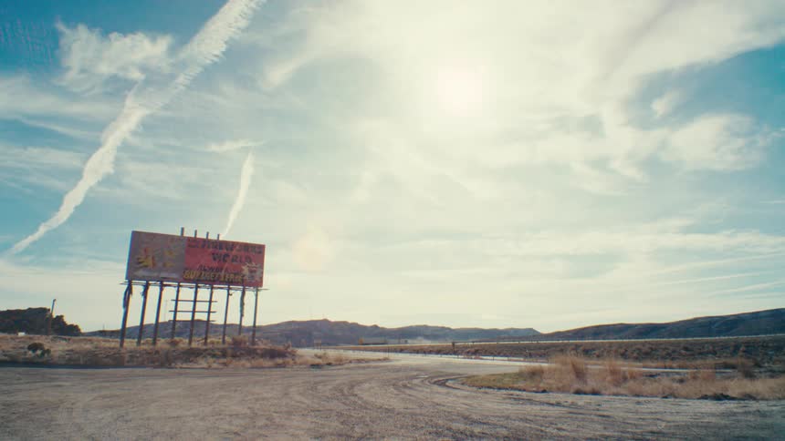A weathered billboard stands alone in a vast open landscape its faded sign contrasting with the clear blue sky and distant hills