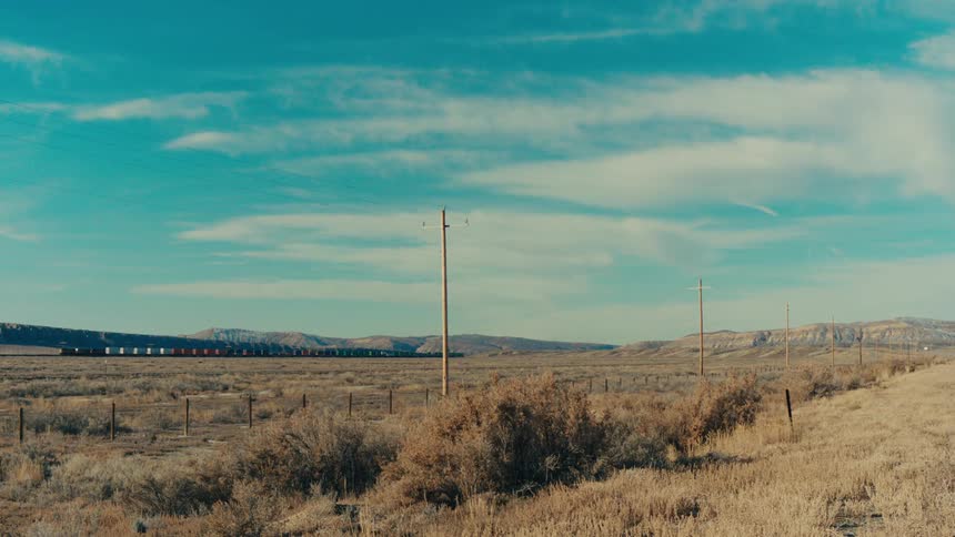 Cargo train passes through rural land with mountains in the distance