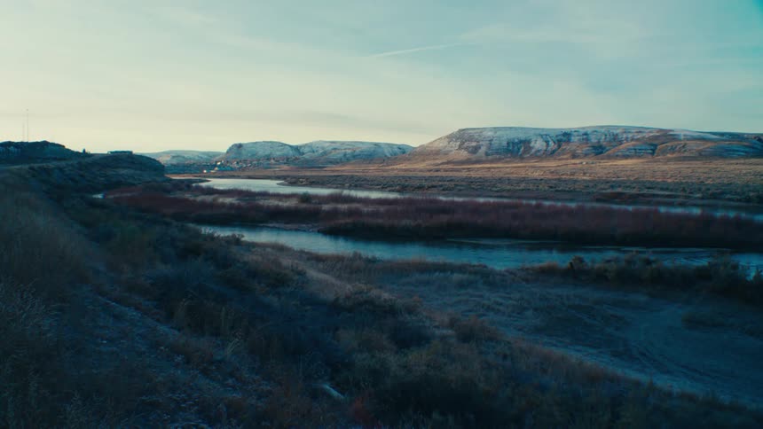 A serene landscape with a wide river winding through a valley surrounded by rolling hills and a distant town under a clear sky