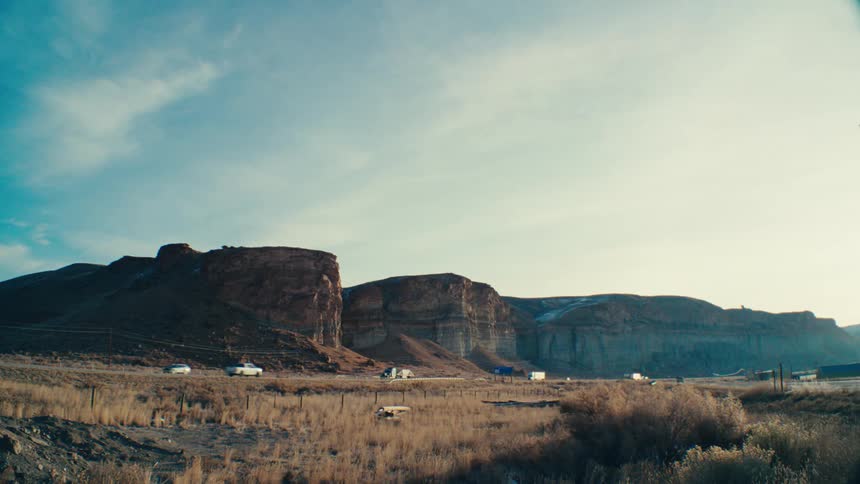 A vast landscape with dramatic rock formations and a highway stretching into the distance under a clear blue sky