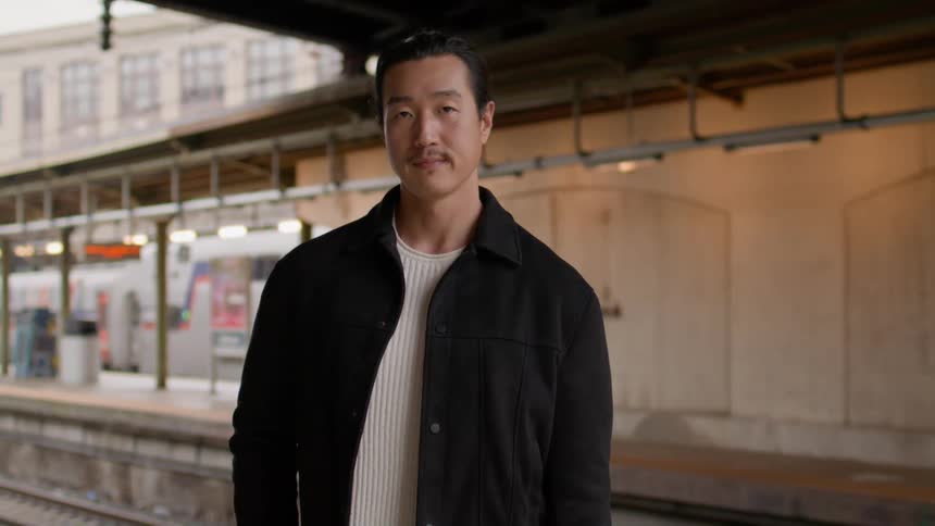 Man in a white shirt and a black jacket in an outdoor subway station
