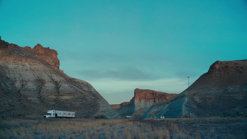 Car and truck traffic on a highway surrounded by mountains and ruins