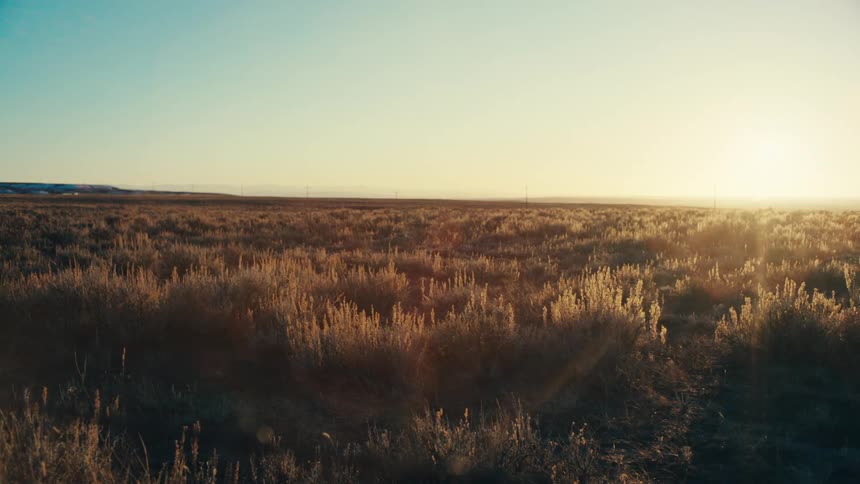A static wide shot of vast plains bathed in the warm light of either sunrise or sunset a distant car is only perceptible due to sunlight reflecting off it on the horizontags