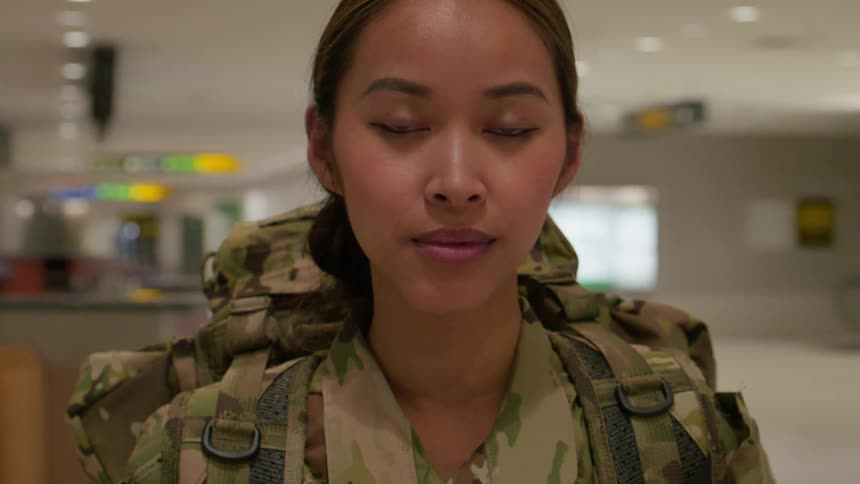 A female soldier in full military uniform carrying a backpack stands tall in a portrait taken at an airport