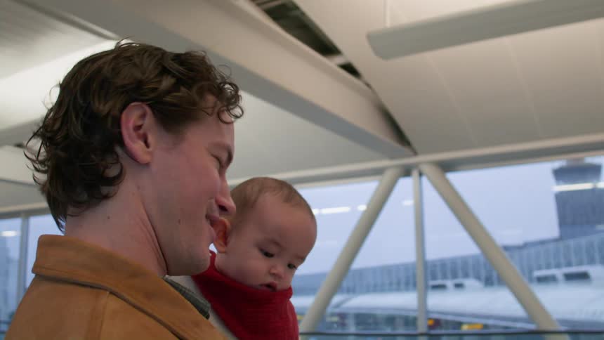 Father with baby in his arms while standing in an airport hallway