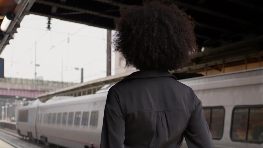 Woman walking through a subway station with a train next to her