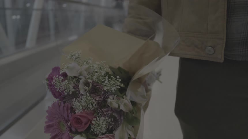 Man holding flower bouquet waiting for someone at an airport terminal