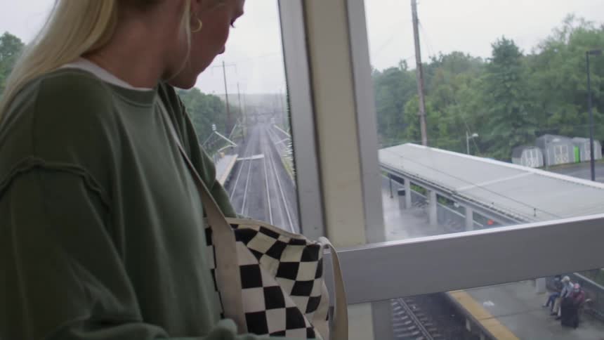 Blonde woman taking a cell phone out of her bag while standing in a terminal hallway
