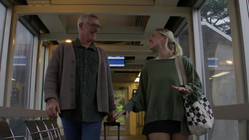 Man with a suitcase talking to a woman next to him as they walk down a terminal hallway