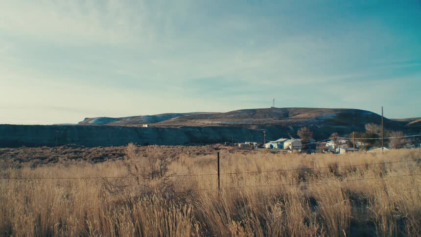 A small town nestles against a hillside surrounded by a vast open landscape under a clear blue sky