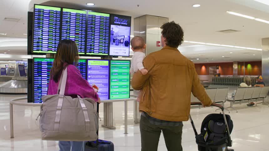 Young family traveling with a baby looking at airport departure screens for thier gate