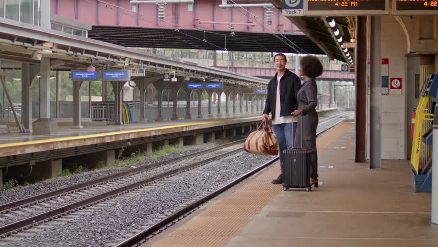 A young couple stands on a train platform waiting for a train to arrive