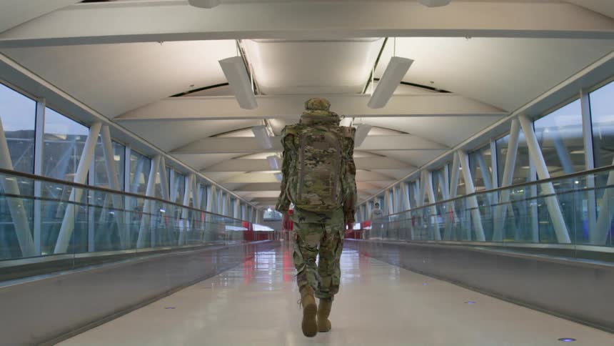 Person in military uniform walking down an airport corridor