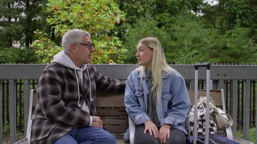 Father and daughter sit on a bench at the park talking to each other