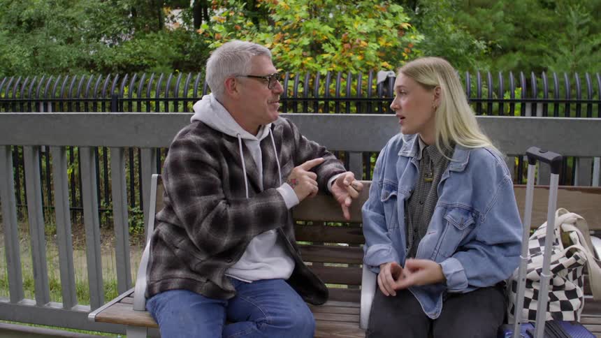 An older person and a younger person sit on a bench on a park