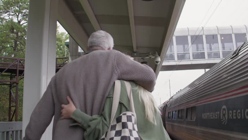 Man hugging a woman as they walk alongside a train at a station