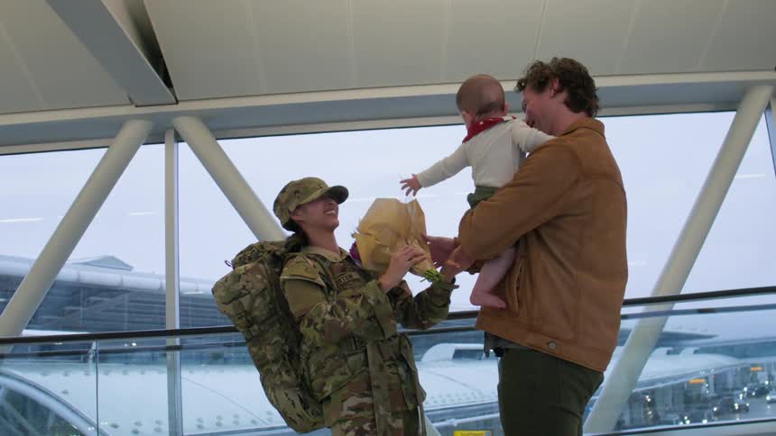 Man holding his baby daughter in his arms and giving a flower to his wife in military uniform