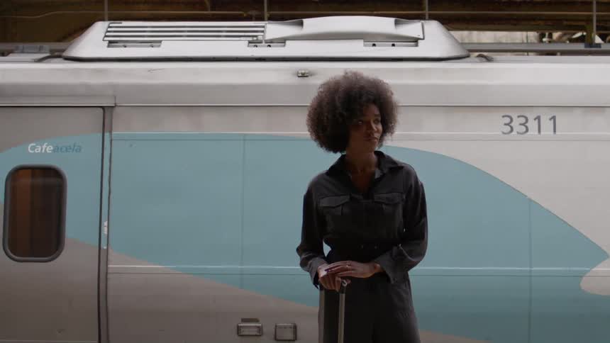 A woman is standing with her luggage in front of a train