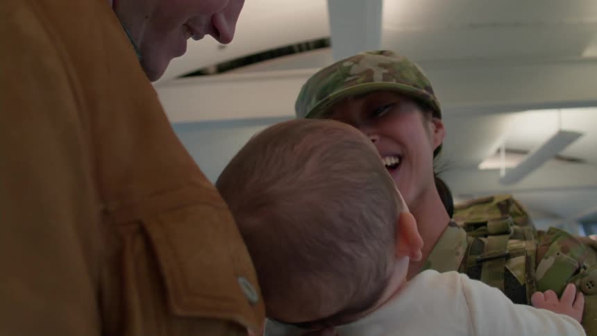 A woman with a hat and militarized clothes is looking at a baby who was in a mans lap and they are happy