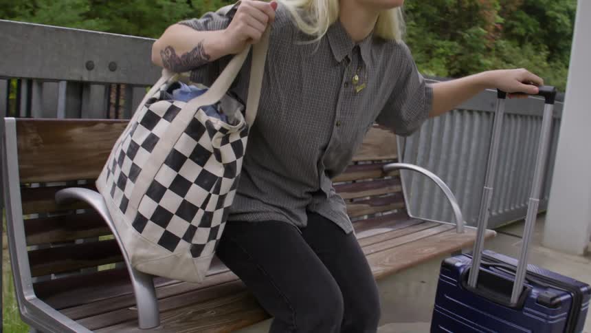 Woman walking with a suitcase in an outdoor subway station and sitting on a wooden bench