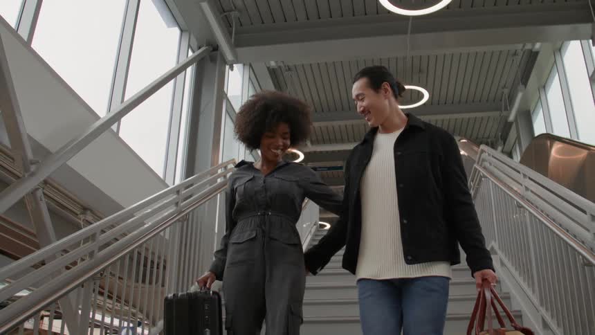 A happy couple walking down the staircase of a train station carrying bags