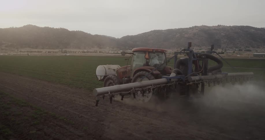 A tractor working in a crop field and the camera zooming in past them