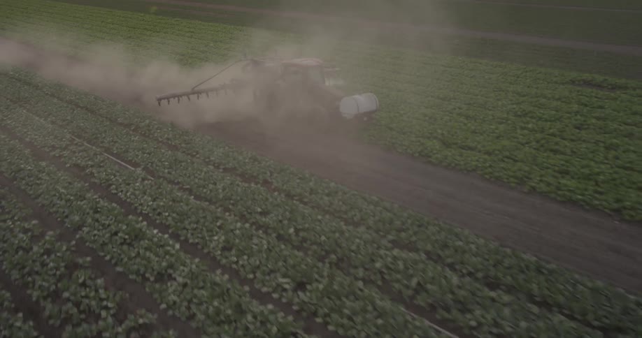 A farmer is spraying his crop being filmed from a drone