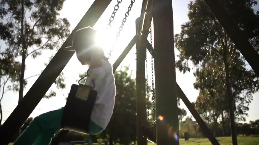 Child swinging on a swing set with the sun shining brightly