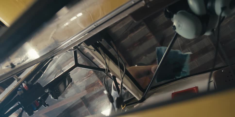 A man standing outside a small aircraft inside a hangar is cleaning the cockpit glass with a cloth