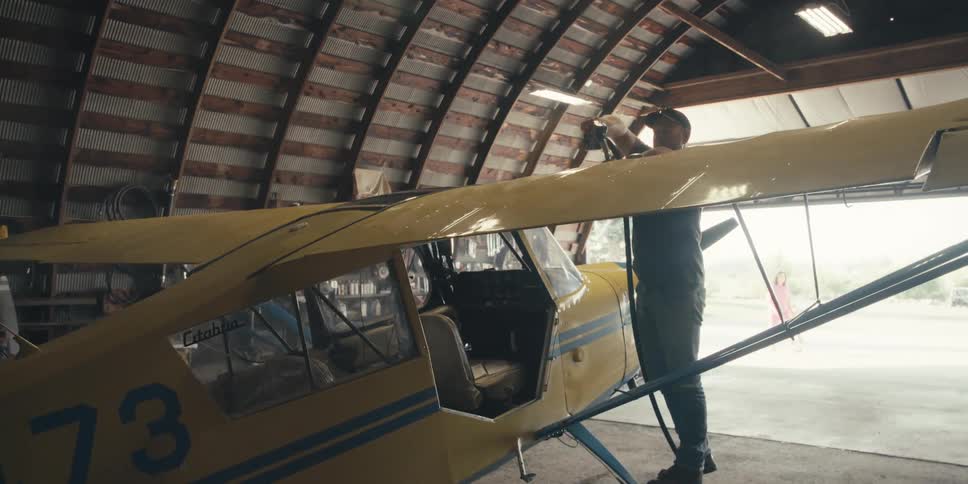 A person fuels up a yellow and blue small aircraft inside a curved roof hangar