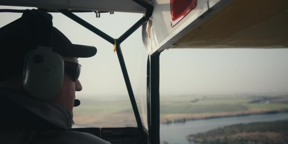 Male pilot wearing a cap and sun glasses in the cockpit of an airplane in midair