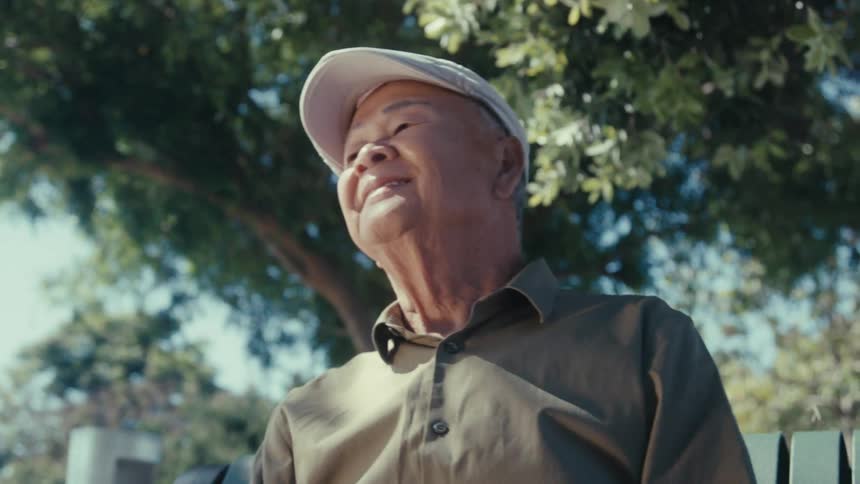 Elderly man in a white beret sitting on a bench under a tree