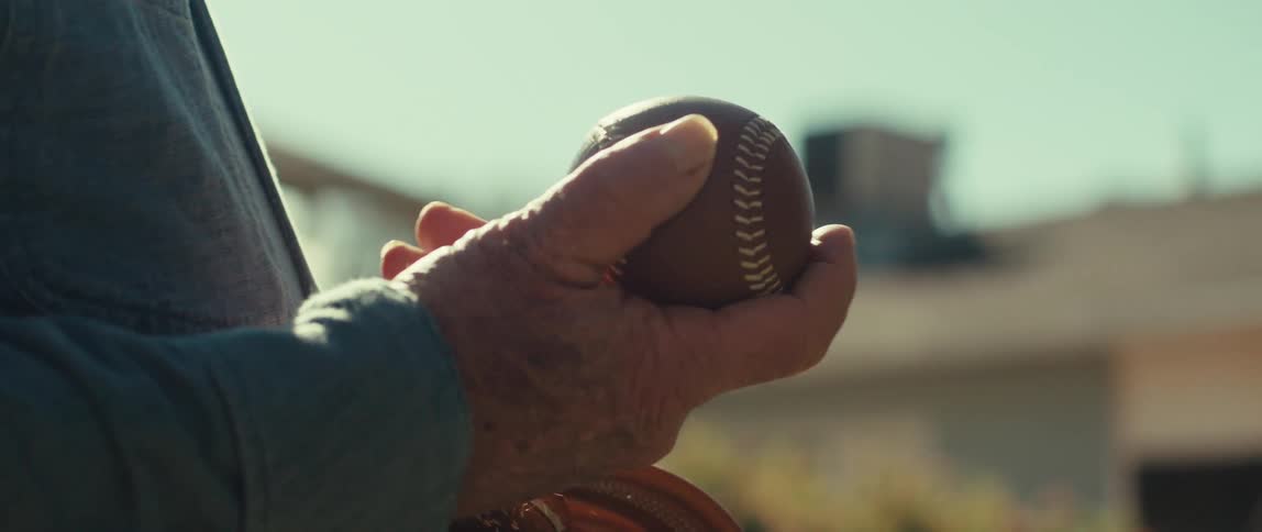 An old persons hand holding a baseball and moving it with his fingers