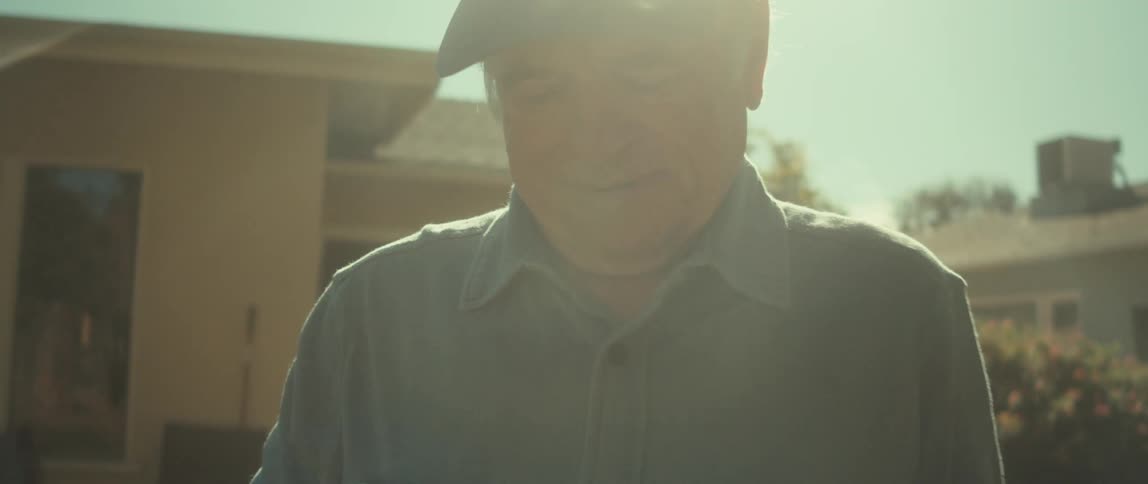 Elderly man in a backyard holding a baseball and a baseball glove