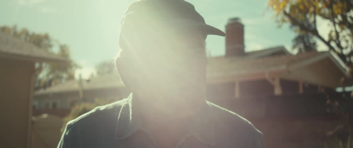 An elderly man is pitching a baseball on a sunny day in his backyard