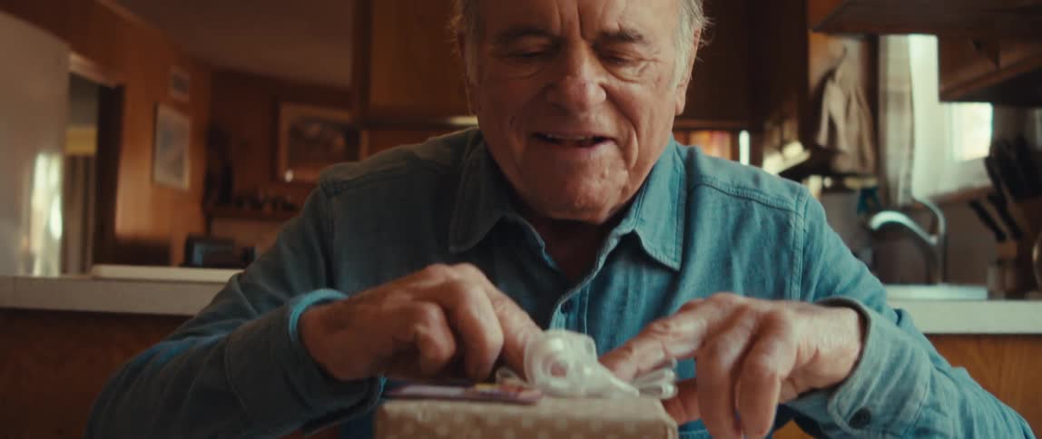 An elderly man places a bow on a wrapped gift box at home