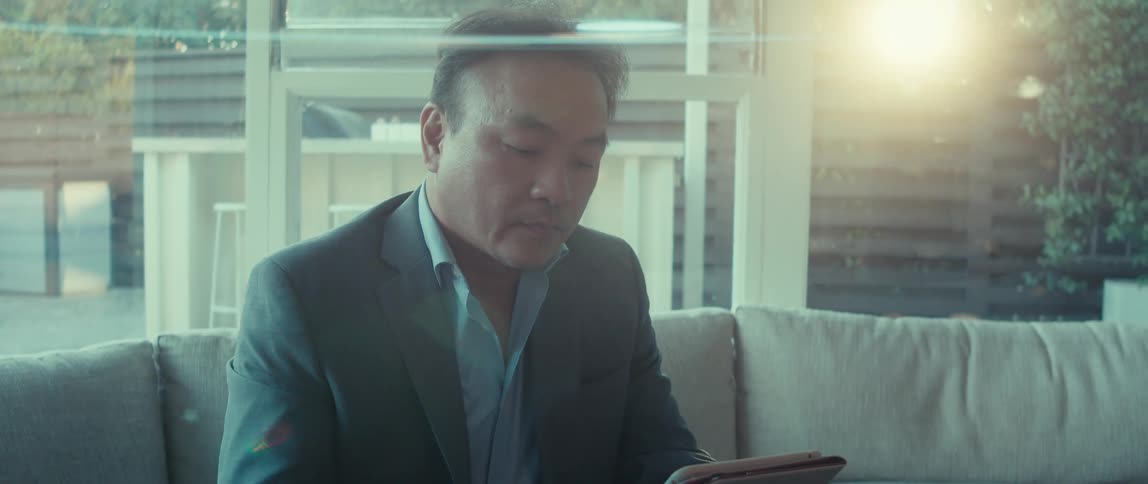 A man in a business suit sits at home on a sunny morning using a tablet
