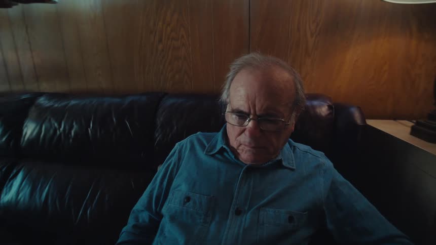 An elderly man is sitting on a couch at home reading documents