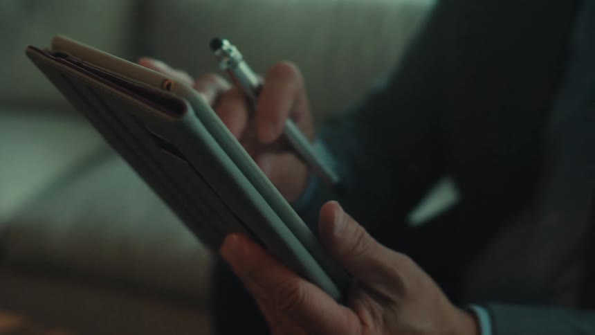 A person interacts with a tablet device using a stylus holding it in one hand while manipulating the screen with the other