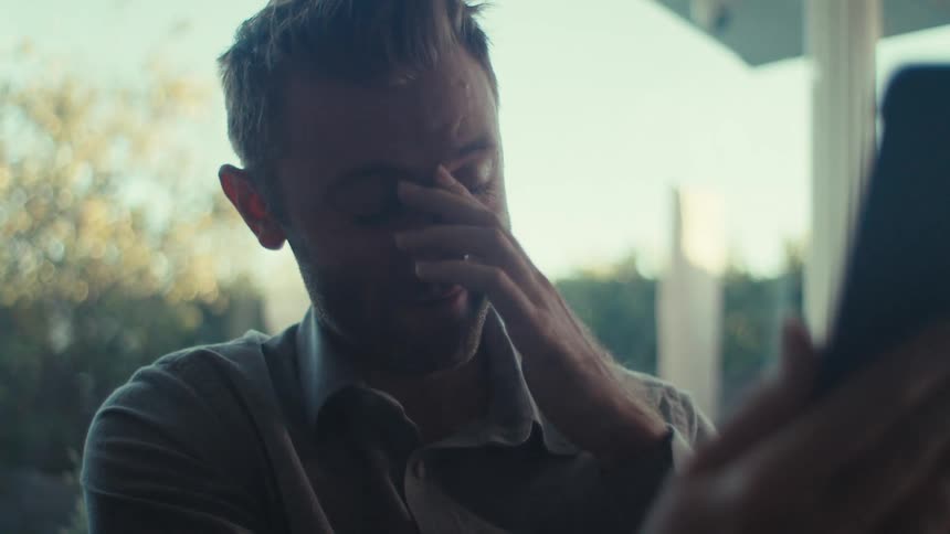 A man wearing a shirt is having a video call on a tablet talking and laughing
