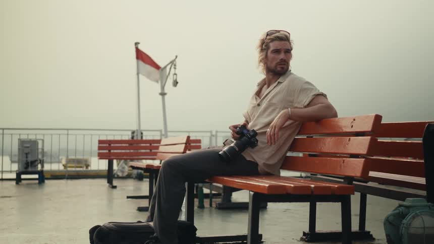 A man sits on a park bench and takes a picture of his shoe using a professional camera with a large lens